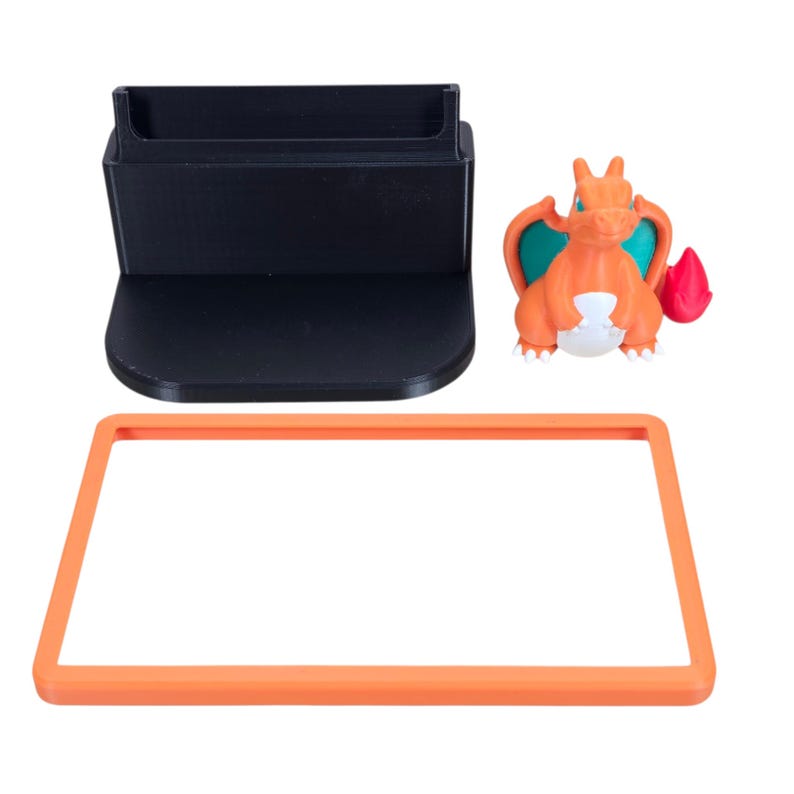 May include: A black plastic stand with a curved base and a slot, an orange rectangular frame, and an orange and white Charizard figurine with teal wings and a red flame.