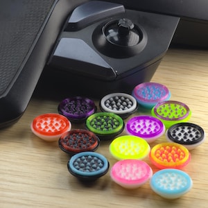 May include: A collection of colorful, round accessories with textured surfaces, likely for a gaming controller. The accessories are in various colors, including red, purple, green, and blue, and are arranged on a wooden surface.