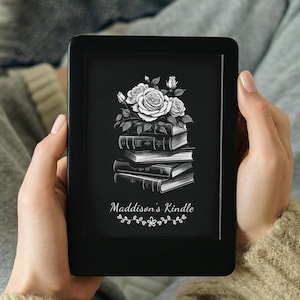 Könnte beinhalten: Ein schwarzer E-Reader mit einem weißen Blumenmuster und dem Text "Maddison's Kindle" auf dem Bildschirm.