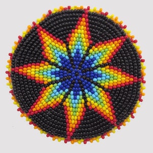 May include: A round, beaded coaster with a starburst design. The center of the star is blue, with rays of yellow, orange, red, and green. The background is black, and the edge is trimmed with red and yellow beads.