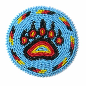 May include: A round beaded design with a blue background and a black bear paw print in the centre. The paw print is outlined in red and yellow beads.