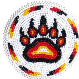 May include: Circular beaded coaster with a bear paw motif. The paw print is black, red, and yellow, on a white beaded base. The border features alternating red, yellow, and black beads.