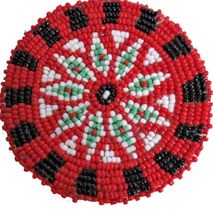 May include: A round beaded coaster with a red, white, green, and black design. The center of the coaster has a black circle surrounded by white beads. The outer edge of the coaster has a black and red design.