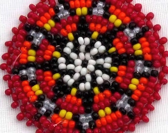 May include: A circular beaded design with a central white and black pattern surrounded by concentric rings of red, orange, yellow, and silver beads.