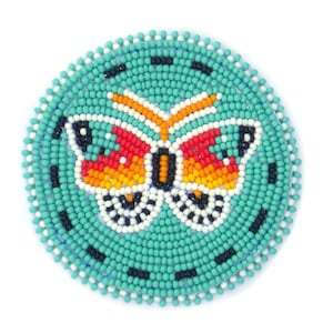 May include: A round beaded ornament with a turquoise background and a colorful butterfly design. The butterfly has orange, red, yellow, black, and white beads.