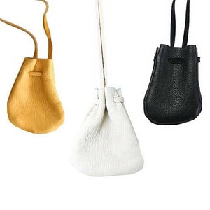 May include: Three small drawstring bags made of leather. The bags are hanging from their straps. The bags are yellow, white, and black.