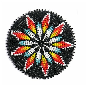May include: A round, black beaded coaster with a colorful starburst design. The starburst features red, yellow, white, and blue beads. The coaster is likely handmade and has a detailed, textured surface.