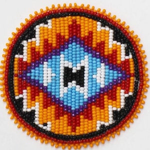 May include: Round beaded ornament with a geometric design. The center features a light blue diamond shape with a black square. The design is surrounded by red, orange, white, and black beads. The outer edge is lined with orange beads.