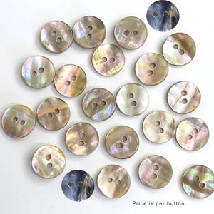 May include: A collection of 20 iridescent mother of pearl buttons with two or three holes. The buttons are various shades of brown, beige, and white.