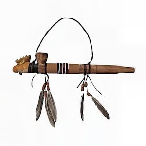 May include: A handcrafted wooden pipe with a carved moose head on one end. The pipe features a wooden bowl, decorative bands with red and black stripes, and hanging feathers with beads. A black cord is attached for hanging.
