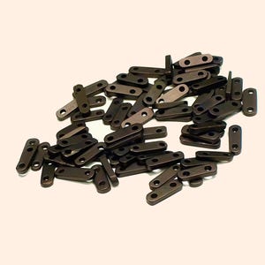 May include: A collection of small, rectangular metal pieces with rounded ends and two holes. The pieces are a dark bronze color and appear to be hardware components, scattered on a light background.