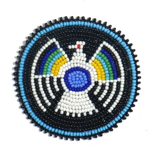 May include: A round beaded design featuring a white bird with blue, yellow, green, and red accents. The bird is surrounded by a black background with a blue and turquoise border.