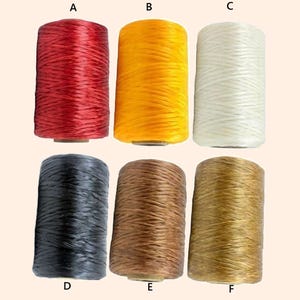 May include: Six spools of waxed thread in various colors. The colors include red, yellow, white, black, brown, and gold. The spools are cylindrical and appear to be made of a woven material, suitable for crafting and sewing projects.