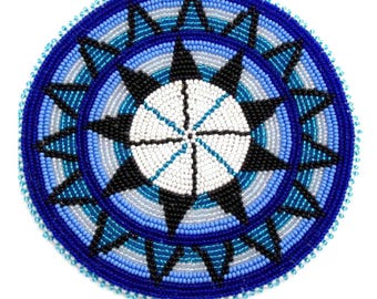 Könnte beinhalten: Rundes Perlendesign in Blau-, Weiß- und Schwarztönen. Das Zentrum zeigt ein weißes Sternmuster, umgeben von konzentrischen Ringen aus blauen und grauen Perlen. Der äußere Rand ist tiefblau mit einem Perlenrand. Dieser handgefertigte Artikel ist wahrscheinlich ein Untersetzer oder ein dekoratives Stück.