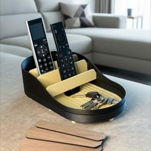 May include: A black and beige remote control and key organizer. The organizer has a curved shape with multiple compartments for remotes and keys. The interior is beige, and the exterior is black. Several keys and remotes are inside the organizer.