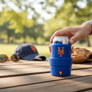 Pode incluir: Um refrigerador de latas azul com detalhes em laranja e o logotipo do New York Mets cont&eacute;m uma lata prateada. Um bon&eacute; de beisebol, &oacute;culos de sol e uma luva de beisebol est&atilde;o em uma mesa de madeira.