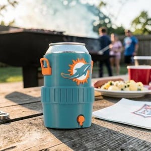 May include: A teal can cooler with an orange handle and a Miami Dolphins logo. The cooler is on a wooden table with food and a bottle opener. People are in the background near a barbecue.