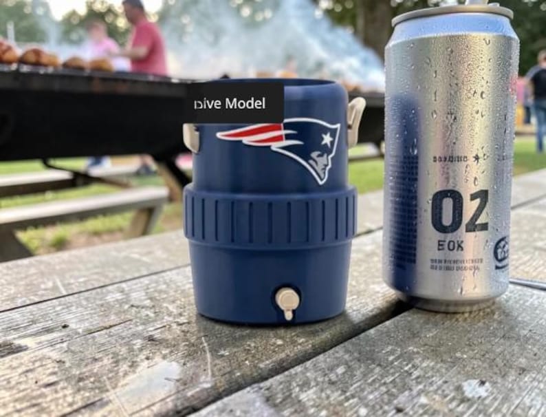 May include: A navy blue drinks cooler with the New England Patriots logo next to a silver can with condensation. The cooler has a white tap and handles. The can has the number "02" printed on it.