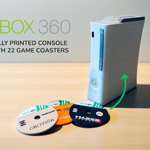 May include: White Xbox 360 console with a green arrow pointing to a set of game coasters. The coasters are round and feature game titles like "Oblivion" and "Mass Effect." Text on the image reads "XBOX 360, FULLY PRINTED CONSOLE WITH 22 GAME COASTERS."