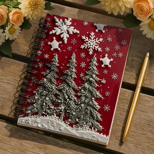 May include: A red spiral-bound notebook with a winter holiday theme. The cover features embossed white snowflakes and Christmas trees. A gold pen rests beside the notebook on a wooden surface, with flowers in the background.