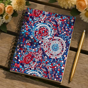 May include: Spiral-bound notebook with a vibrant, colorful dot pattern in red, white, and blue. A gold pen rests beside the notebook on a wooden surface, with flowers in the background. The notebook's design features concentric circles.