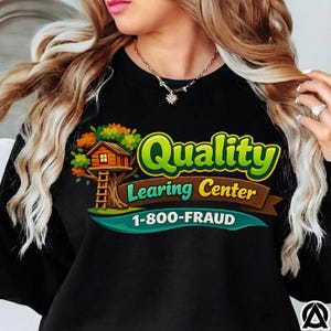 May include: Black crew neck sweatshirt with a colorful graphic. The graphic features a treehouse with the words "Quality Learing Center" and the phone number "1-800-FRAUD" in a playful font. The design includes green, brown, orange, and yellow colors.