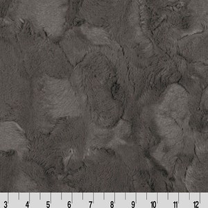May include: A close-up of a gray faux fur fabric with a soft, plush texture. The fabric has a subtle marbled pattern.