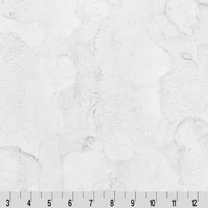 May include: White faux fur fabric with a soft, fluffy texture. The fabric has a subtle, irregular pattern.