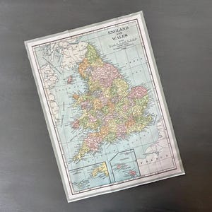 May include: A vintage map of England and Wales, featuring detailed geographical information. The map is printed on aged paper and framed with a thin, transparent border. The map includes place names, roads, and color-coded regions.
