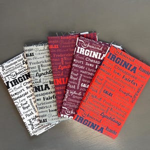 May include: Four fabric items with the word "VIRGINIA" and various city names printed on them. The items are in shades of red, burgundy, and black and white. The text is in a bold, sans-serif font.