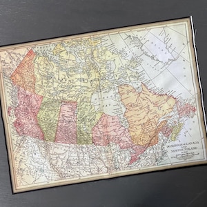May include: A vintage map of Canada and Newfoundland, featuring detailed cartography with a cream-colored background and colorful provinces. The map is framed with a black border and includes the text "Dominion of Canada and Newfoundland".