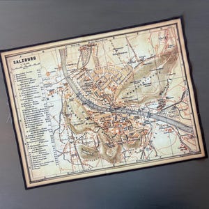 May include: An antique map of Salzburg, Austria, with detailed streets, buildings, and geographical features. The map is in sepia tones with a black border, and the word "Salzburg" is at the top.