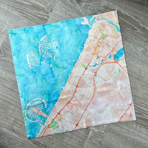 May include: A watercolor painting of a map of Dubai, featuring the city's skyline and surrounding desert landscape. The painting is done in shades of blue, green, and brown, with a white background.