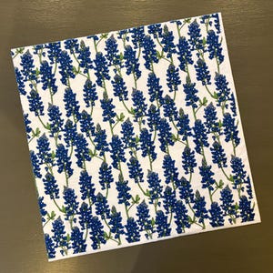May include: White fabric with a repeating pattern of blue Texas bluebonnet flowers. The flowers are stylized and have a green stem.
