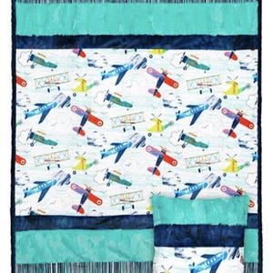 May include: A baby quilt and pillow set featuring a colorful airplane pattern on a white background. The quilt has a teal border and stripes, with a matching pillow. The airplanes are red, blue, and yellow.