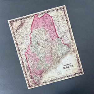 May include: Antique map of Maine with pink and white coloring, featuring intricate details and a decorative border. The map is titled "Johnson's Maine" and is set against a dark gray background.