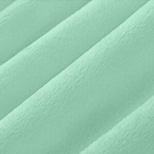 May include: Close-up of a soft, mint green fabric with a plush texture. The material is quilted with diagonal lines, creating a ribbed effect. The fabric has a slight sheen, suggesting a luxurious feel.