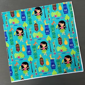 May include: A turquoise fabric with a repeating pattern of hula girls, tiki gods, palm trees, and pineapples. The fabric has a white border.