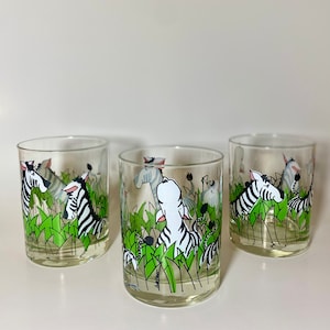 Puede incluir: Tres vasos de vidrio transparente con un diseño de cebra y hojas de la selva. Los vasos están llenos de un líquido blanco.