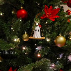 A side view of a white Santa ghost on a brown swing ornament hanging on a holiday Christmas tree with lights in the background.