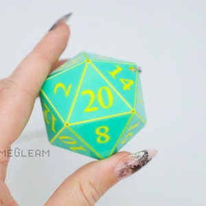 May include: A turquoise 20-sided die with yellow numbers. The die is made of plastic and has a geometric shape.