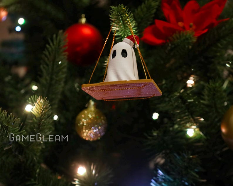 A bottoms up view of a white Santa ghost on a brown swing ornament hanging on a holiday Christmas tree with lights in the background.