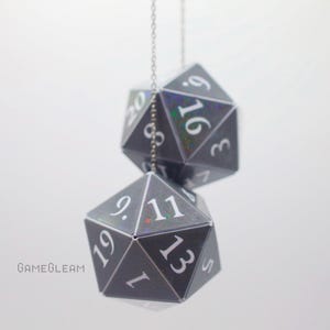 May include: Two black and silver iridescent dice ornaments hanging from a silver chain. The dice are numbered 1-20.