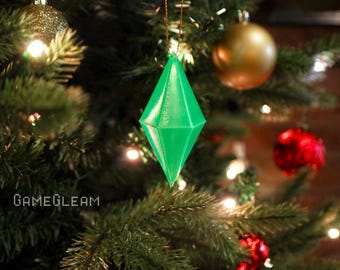 May include: A bright green, geometric Christmas ornament hangs from a tree. The ornament is diamond-shaped with multiple facets. Other ornaments on the tree include gold and red spheres. The tree is a lush green, with lights.