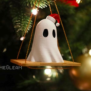 A close up view of a white Santa ghost on a brown swing ornament hanging on a holiday Christmas tree with lights in the background.