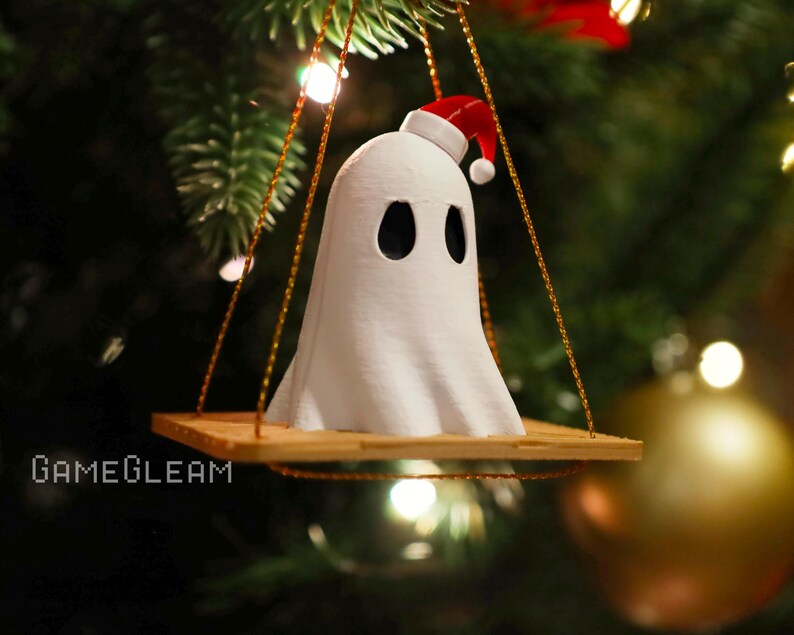 A close up view of a white Santa ghost on a brown swing ornament hanging on a holiday Christmas tree with lights in the background.