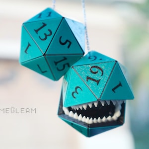 May include: Two teal blue dice with black numbers hanging from a string. The dice are shaped like a 20-sided die and a 12-sided die. The 20-sided die has a set of teeth on the bottom edge.