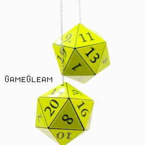 May include: Two bright yellow twenty-sided dice hanging from a thin silver chain. Each die features black numbers printed on its triangular faces. The text GAMEGLEAM is visible in a pixelated black font to the left of the upper die.