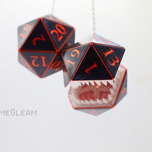 May include: Two black and red dice with orange numbers hanging from a silver chain. The bottom die is open with a white mouth and teeth.