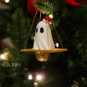 A side view of a white Santa ghost on a brown swing ornament hanging on a holiday Christmas tree with lights in the background.